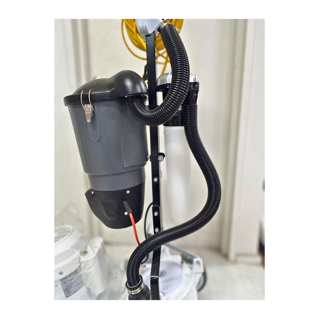 A black wet vacuum cleaner attachment with a flexible corrugated hose, mounted on a black metal stand in an indoor setting.