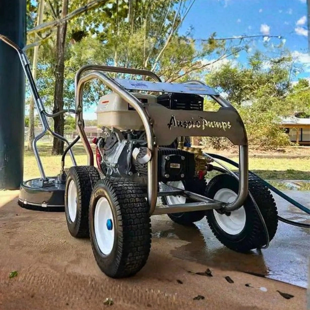 A portable engine-powered pressure washer with four wheels and a metal tub frame, branded 'AngiePumps' on the side panel, parked outdoors on a wet concrete surface with trees and sky in the background.