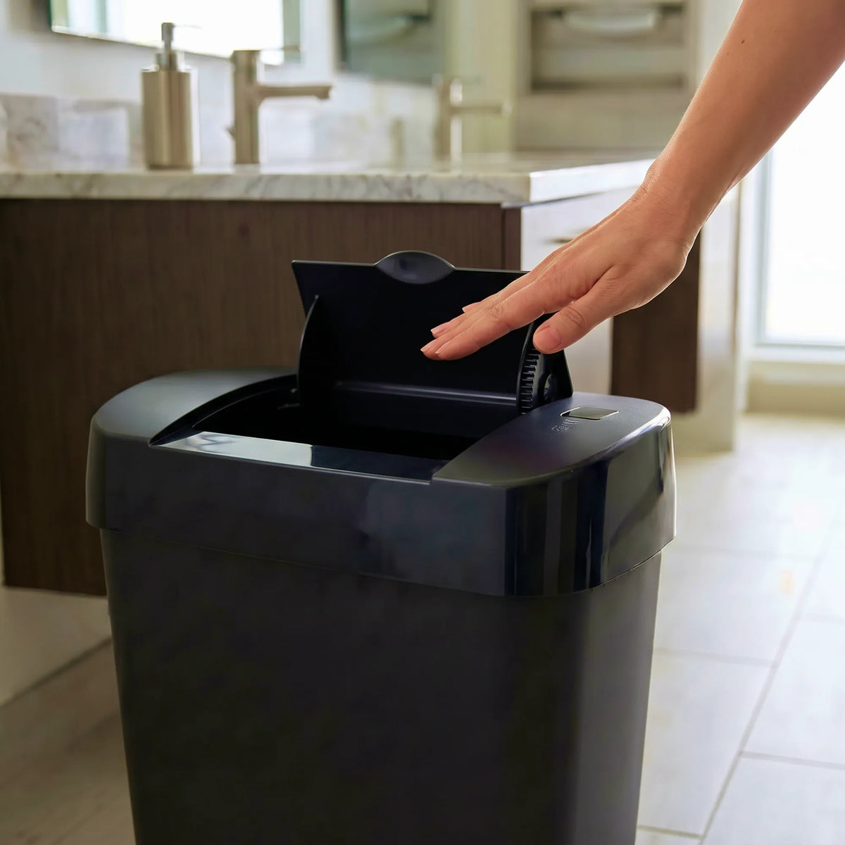 A black automatic感应垃圾桶 in a modern bathroom, with a hand reaching to open the lid.