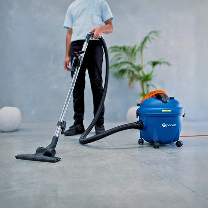 A person using a blue and black vacuum cleaner with an orange handle accent in a modern, minimalist room with a gray concrete floor and wall.