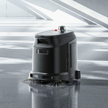 A black robotic floor cleaner with a cylindrical body and rotating bristles at the base, shown on a polished gray floor in a modern interior space with bright architectural lines.