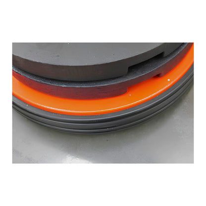 Close-up of a circular product showing a black textured top surface, a bright orange ring, and a dark gray ridged base on a light gray surface.