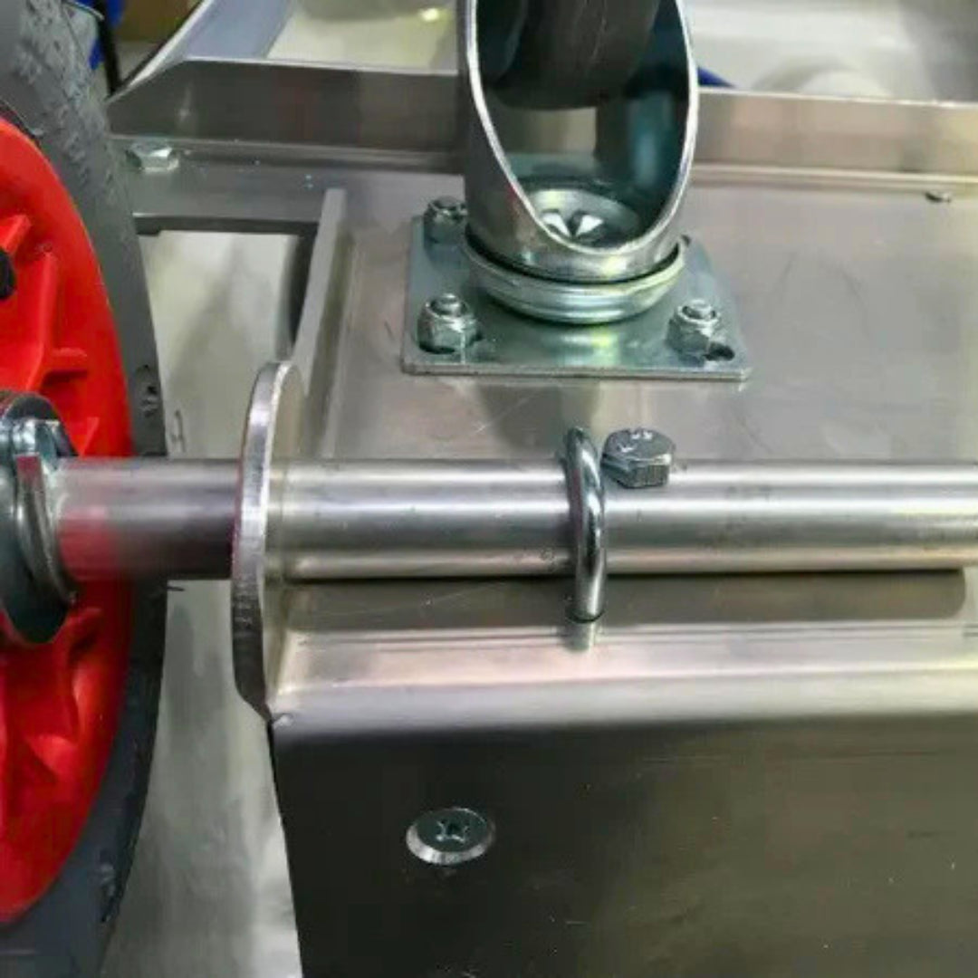 Close-up of a metal mechanical assembly with a red wheel, horizontal metal shaft, bracket, and mounting hardware on a stainless steel frame.
