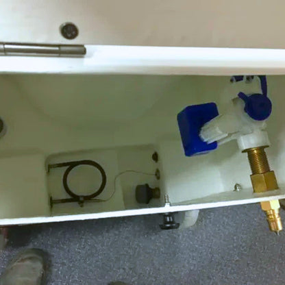 Close-up of a white toilet tank with visible internal plumbing components, including a blue float, brass valve, and metal hose, photographed from below.
