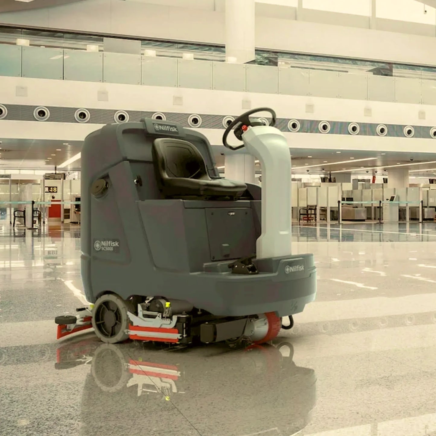 A Nurfocus indoor driverless floor cleaner in gray and white, shown operating on a polished tile floor in a modern airport terminal.