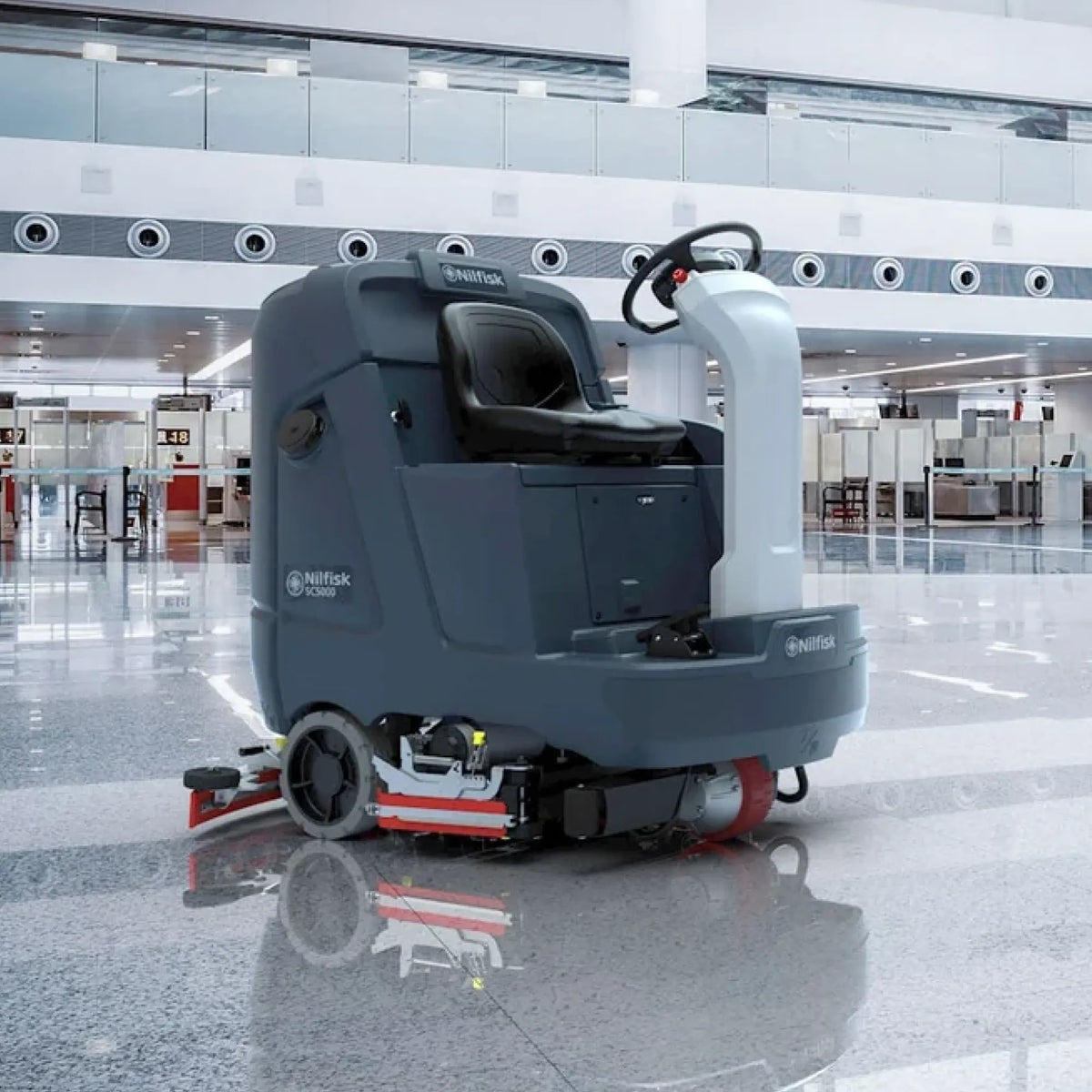 A Nittany Skindustrial P11000 wet floor cleaning machine with a dark gray body, black seat, and red accents, shown in a modern, brightly lit airport terminal.